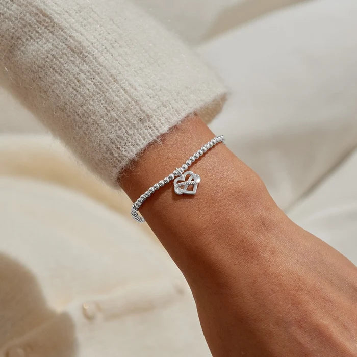 A Littles & Co Family Is A Gift bracelet silver beaded stretch bracelet with interlinked heart charm worn on wrist