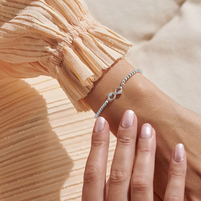 A Littles & Co. A Little Happiest With You bracelet worn on wrist, silver beaded stretch bracelet with infinity heart charm