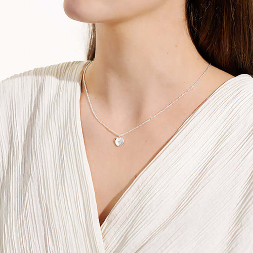 Necklace with a heart-shaped pendant worn by a person in a white outfit