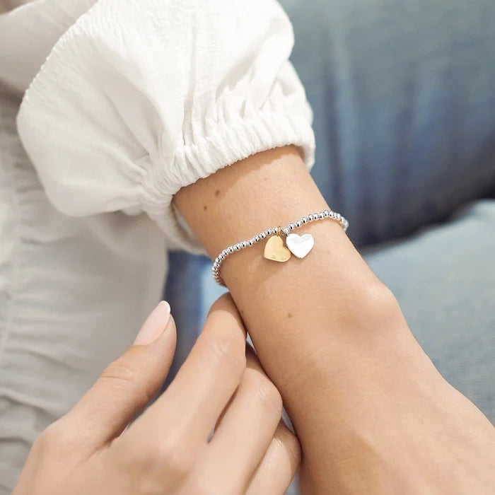 A Littles & Co. Soul Sisters bracelet worn on wrist featuring silver beaded band with gold and silver heart charms