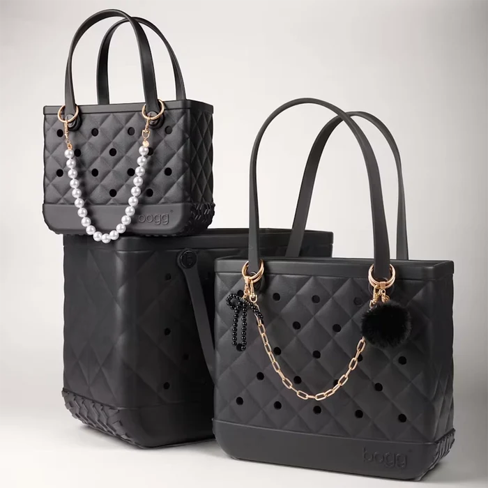Black faux fur pouf keychain with gold hardware attached to a quilted black Bogg Bag as a stylish bag charm