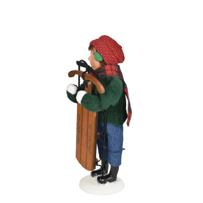 Left side of boy sledding Figurine with  winter clothing holding skis and a sled on a white background
