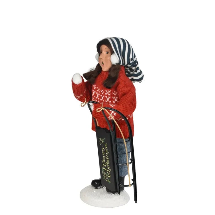 Left side of Byers’ Choice Sledding Girl Caroler holding a green sled marked ‘Merry Christmas