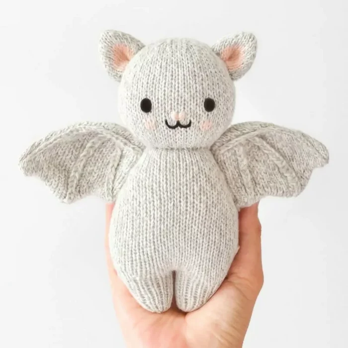 Cuddle + Kind Baby Bat in Grey – small handmade knit bat plush toy held in hand for scale.