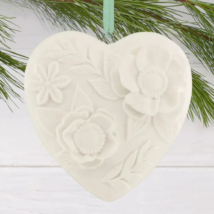 Heart-shaped ceramic ornament with floral patterns hanging on a branch.