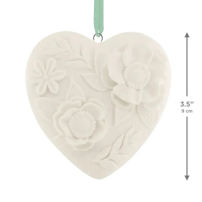 Heart-shaped ceramic ornament with floral patterns and a green ribbon on a white background