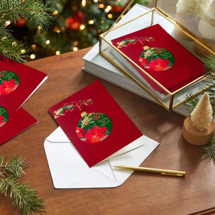 Red Christmas cards with festive designs on a wooden table with a decorated tree in the background.