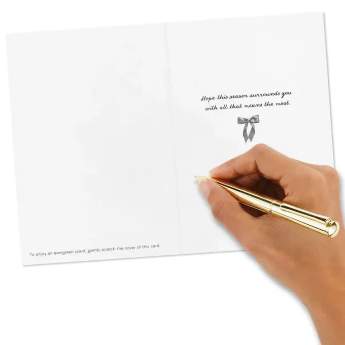 Hand holding a gold pen over a white card with text and a bow design.