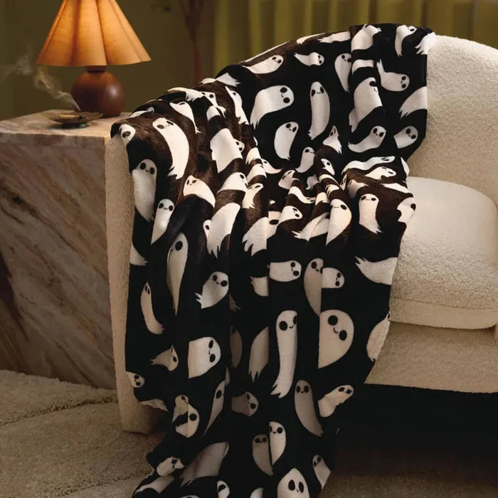 Black blanket with white ghost pattern draped over a chair in a cozy room.