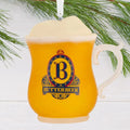 Butterbeer mug ornament with a 'B' logo on a pine branch against a white background