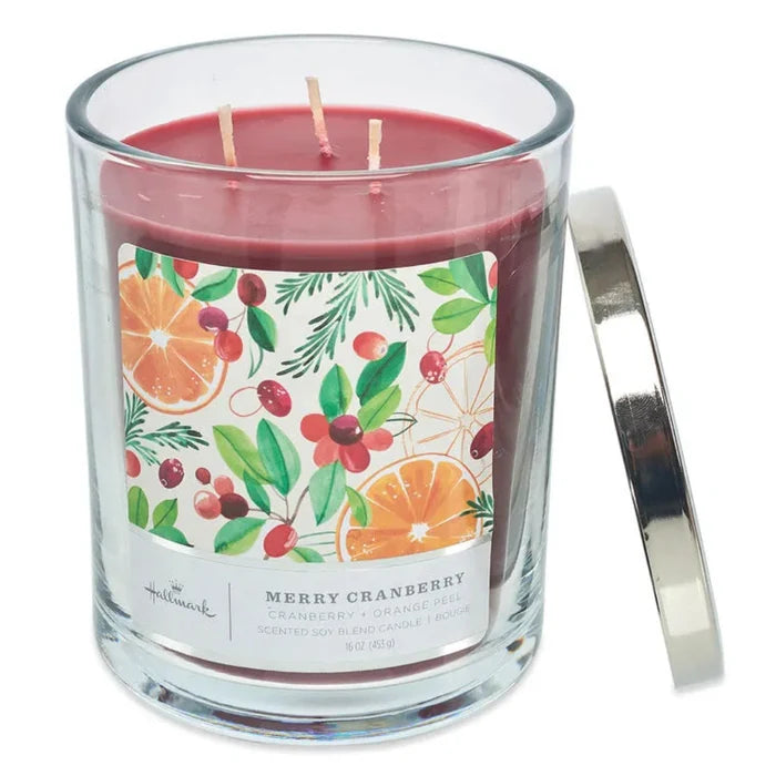 Candle with a decorative label featuring cranberry and orange fruits and a silver lid on a white background