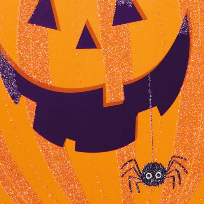 Halloween-themed designed card zoomed up with a jack-o'-lantern face and spider on an orange background