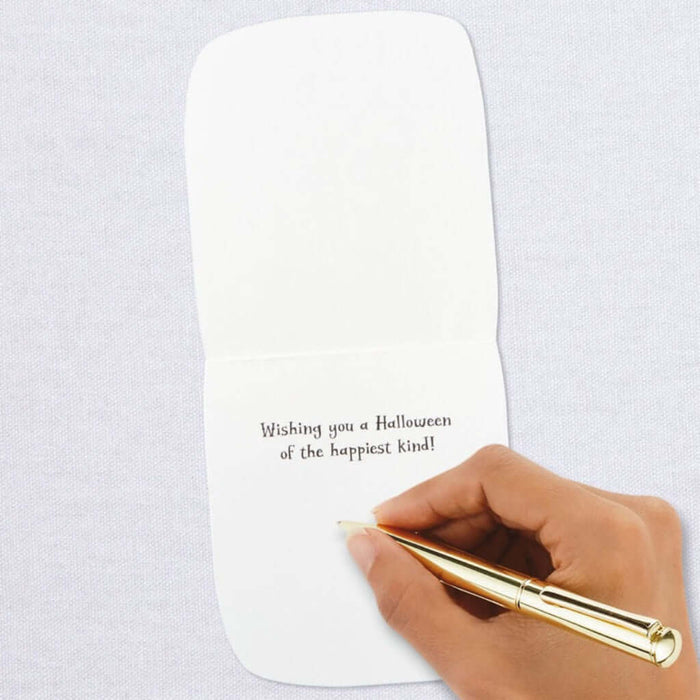 Hand holding a gold pen over a white card with Halloween message on a light grey  background