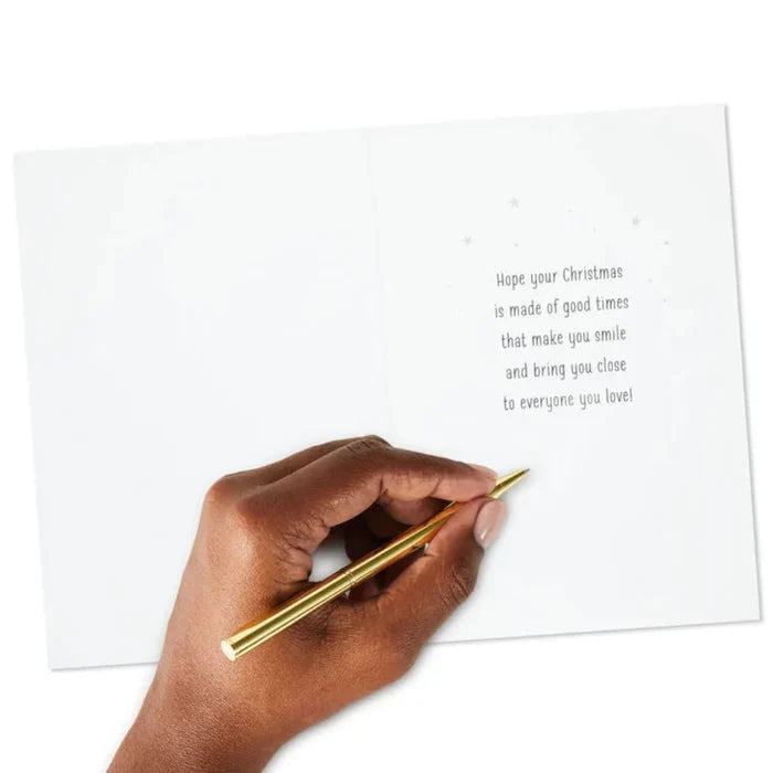 Hand holding a gold pen over a Christmas card with a message.