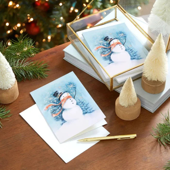 Stack of Christmas cards with a snowman design on a wooden table with decorative items.