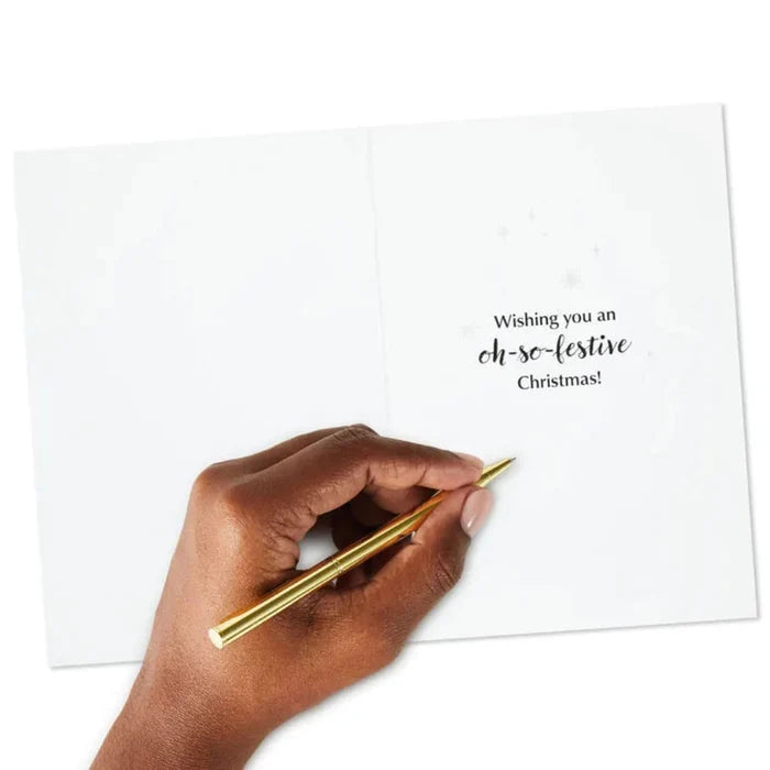 Hand holding a gold pen over a card with a Christmas message.