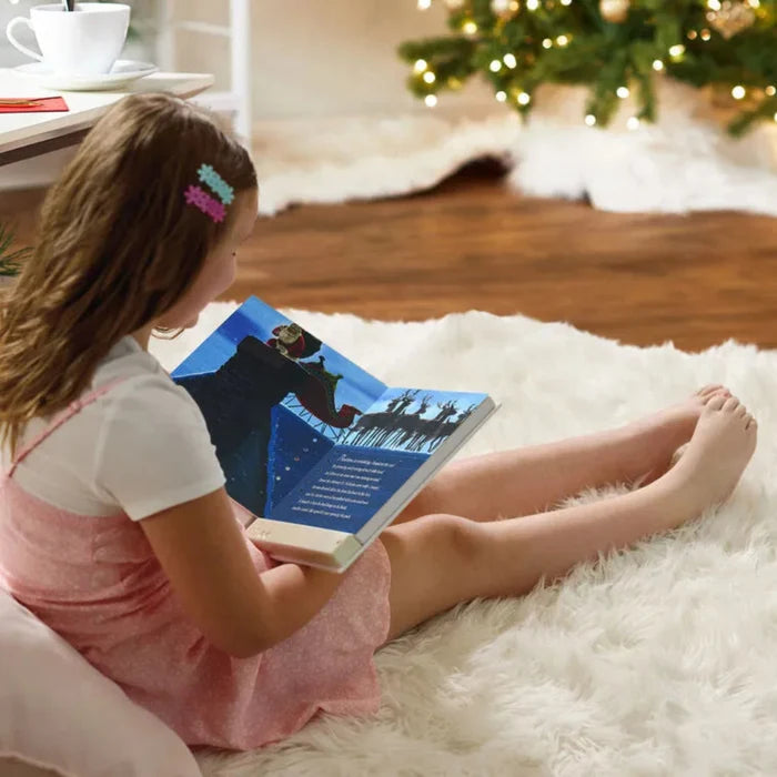 Child reading a book under a decorated Christmas tree