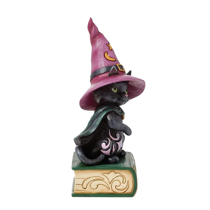 Side view of black cat figurine in witch costume, showing pointed pink hat, cape, and spellbook base.