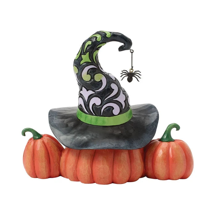 Carved pumpkin jack-o’-lantern wearing a tall patterned witch hat with green band and dangling spider accent.