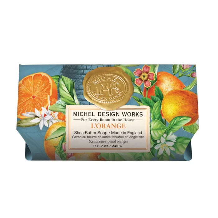 A bar of Michel Design Works L'Orange shea butter soap in floral and orange-themed packaging with a gold seal on the wrapper.