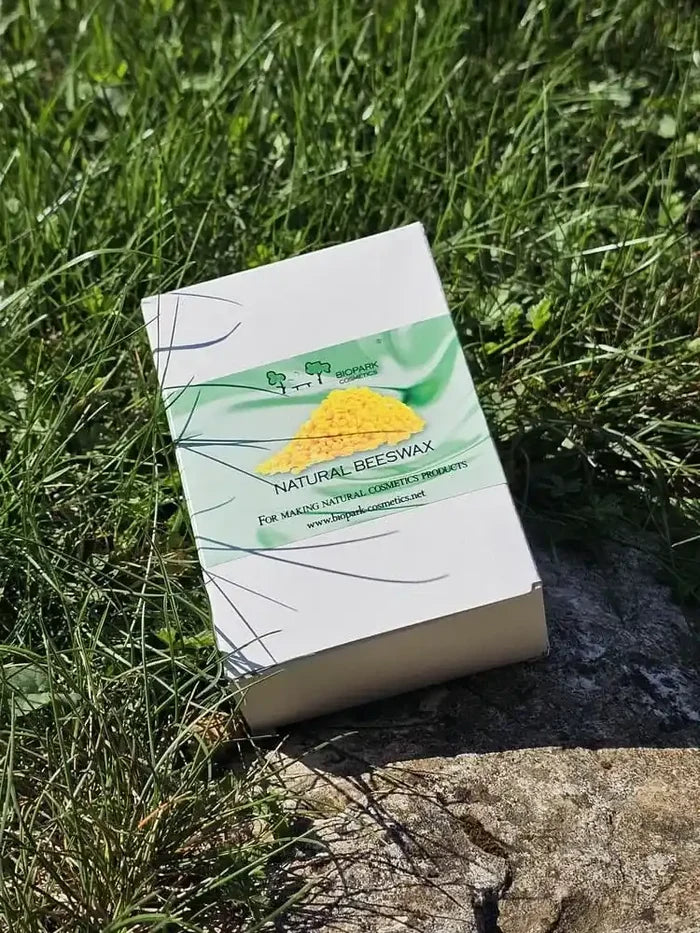 A white box of natural beeswax candles with a green and yellow label, placed on a patch of green grass and stone outdoors.