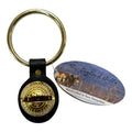 Keychain with black leather strap and gold compass design, accompanied by a New England Bells branded card.