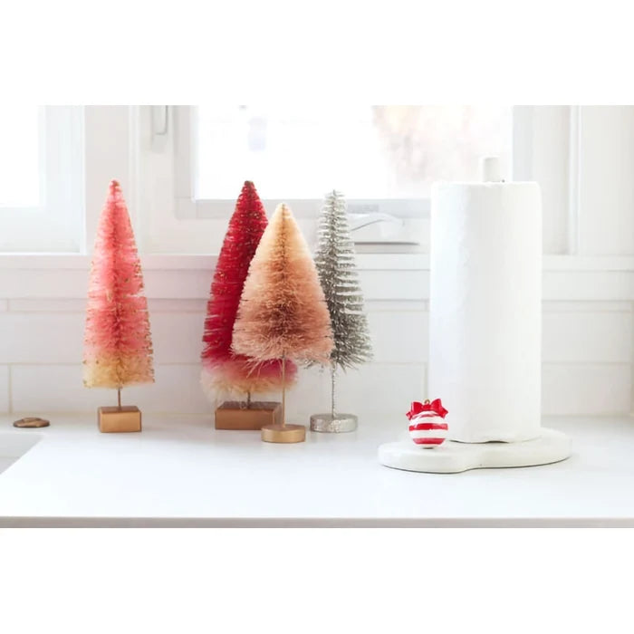 Decorative Christmas trees on a white surface with a lamp in the background