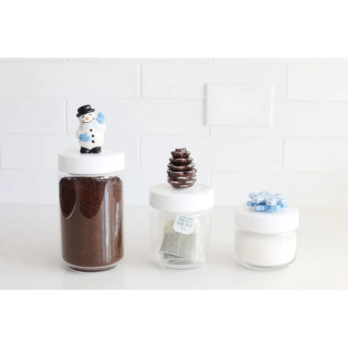 Three glass jars with decorative lids on a white surface