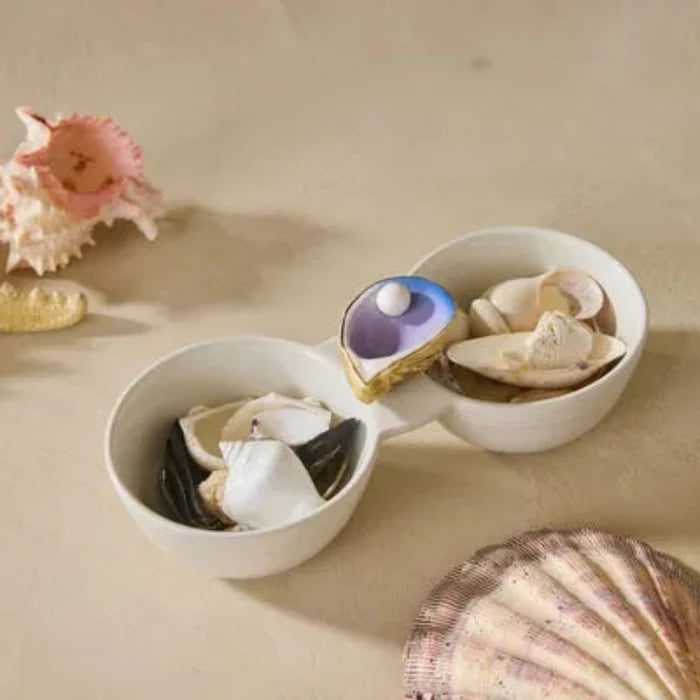 Shell with a pearl Nora Fleming Mini on a sandy surface with starfish and seashells.