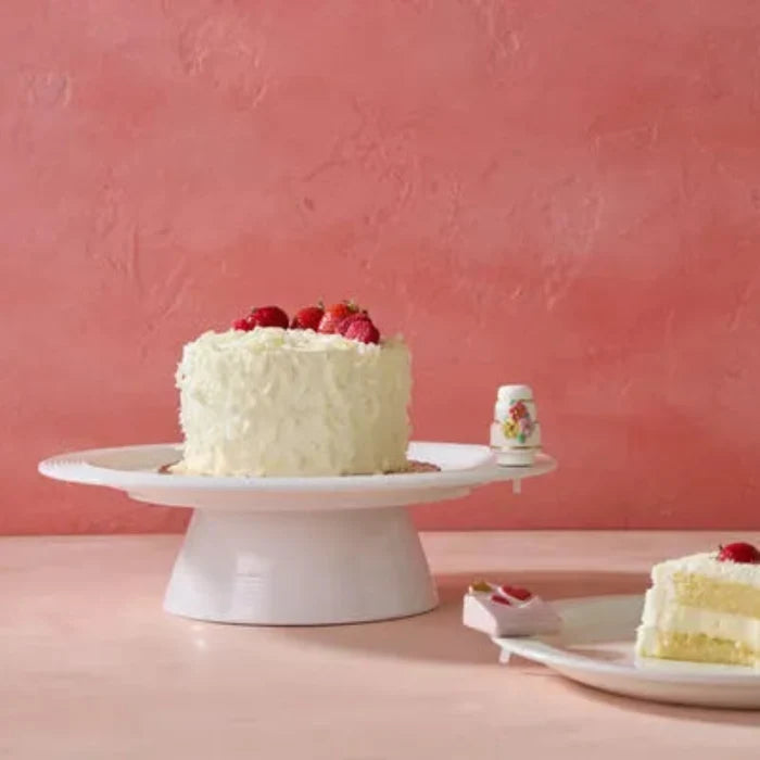 White cake with a cake Nora Fleming Mini on a pink background