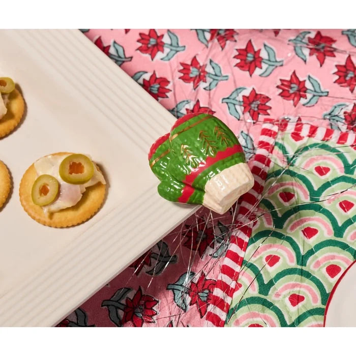 Decorative elf figurine on a floral-patterned surface with crackers and olives.