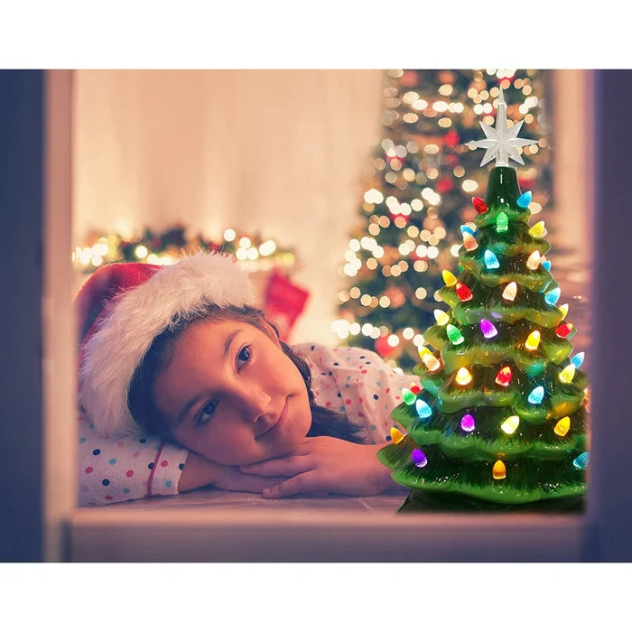 Child wearing a Santa hat looking at a small Christmas tree with lights.