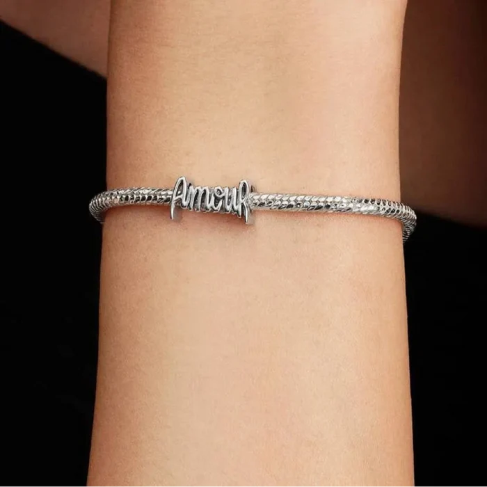 Silver bracelet with 'amour' on a wrist against a dark background