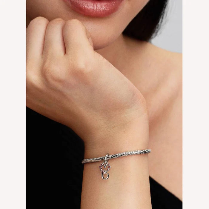 Silver bracelet with a red heart charm on a wrist, close-up view.