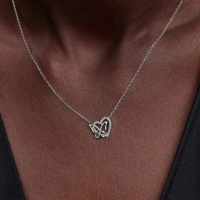 Close-up of a woman wearing a heart and butterfly shaped necklace with a neutral background