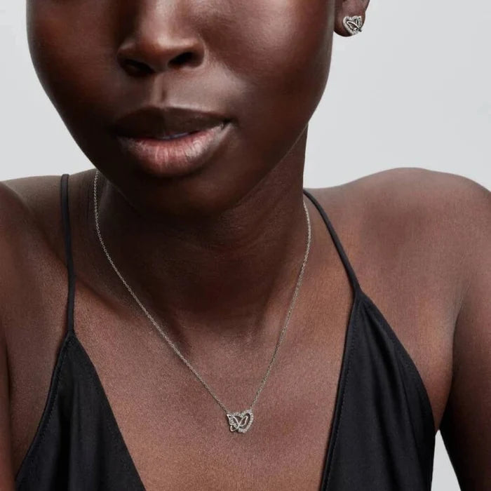 Close-up of a woman wearing a heart and butterfly shaped necklace and a earring with a neutral background