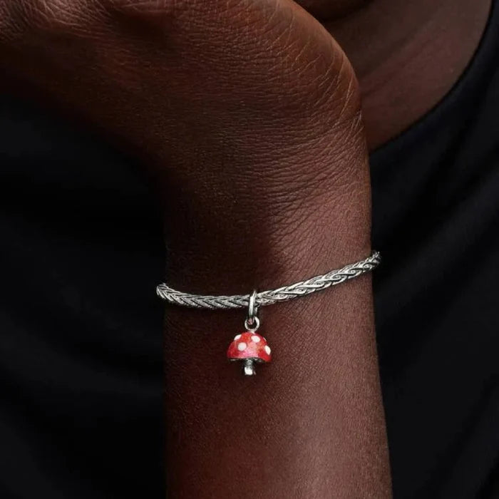 Silver bracelet with a red mushroom charm on a wrist against a dark background