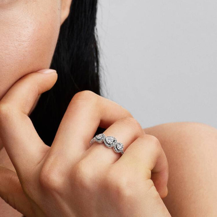 Pandora Halo Heart Trilogy Ring in sterling silver with heart-shaped halo stones worn on a woman's finger.