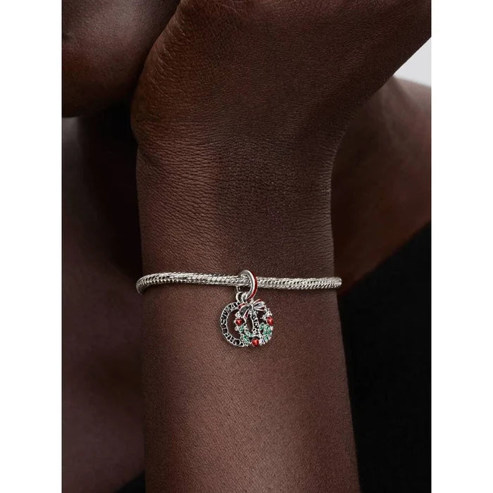 Pandora Holiday Wreath Double Dangle Charm worn on a model’s wrist, showing festive wreath details with red and green accents.