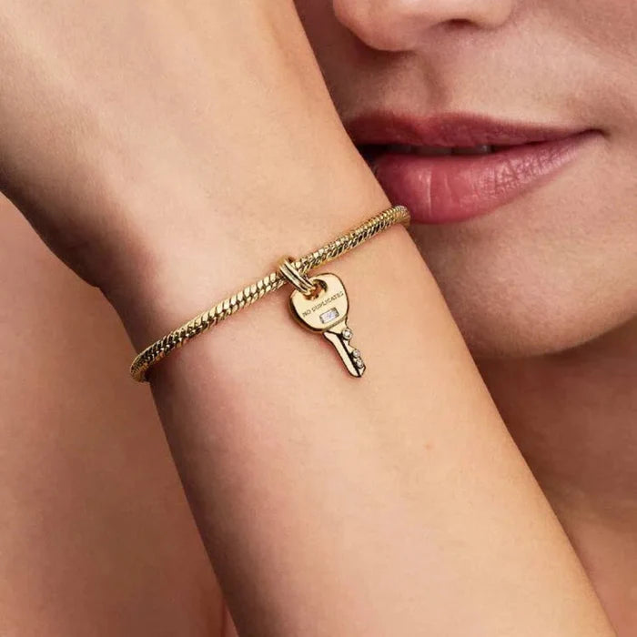 Close-up of a woman's face with a gold bracelet featuring a key charm.