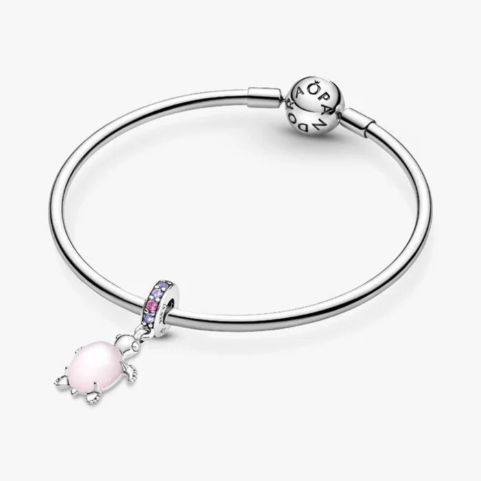 A woman showcases a silver bracelet adorned with a pink turtle charm on her wrist.