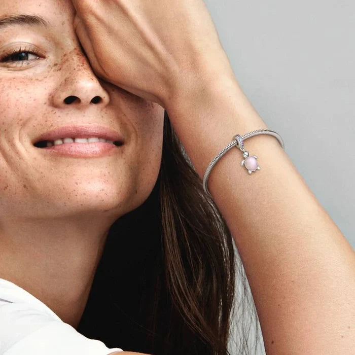 A close-up of a woman's wrist featuring a silver bracelet with a charming pink turtle pendant.