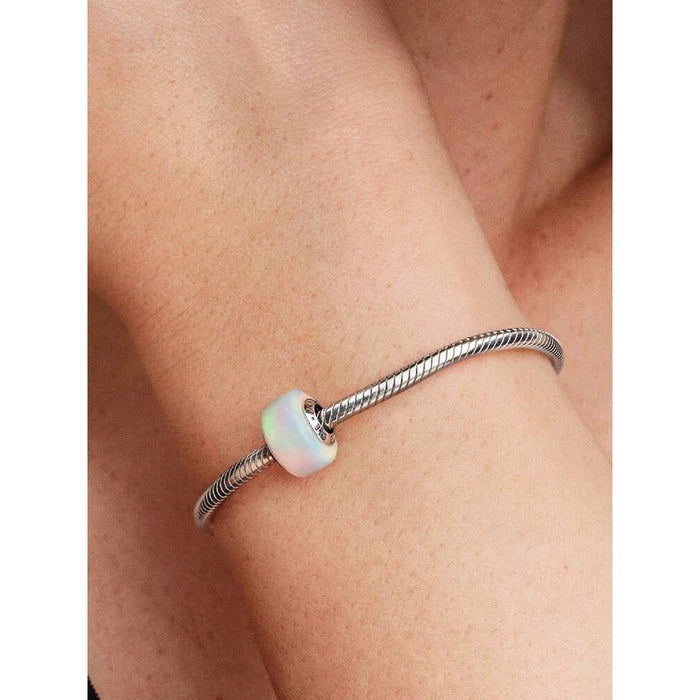 Close-up of a woman's wrist wearing a Pandora bracelet featuring the opalescent Murano glass charm in soft iridescent colors.