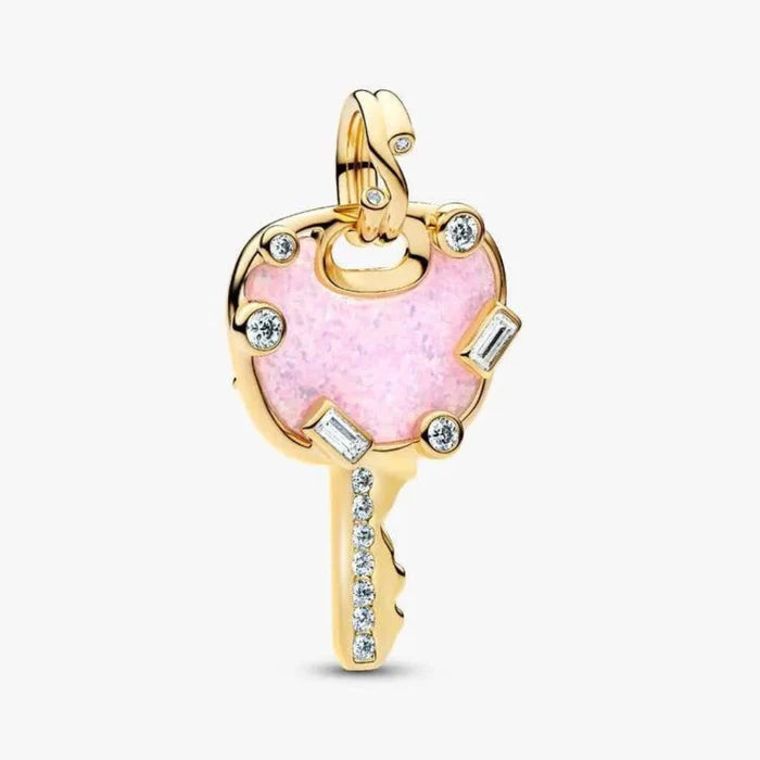 Gold key-shaped pendant with pink heart and clear stones on a white background