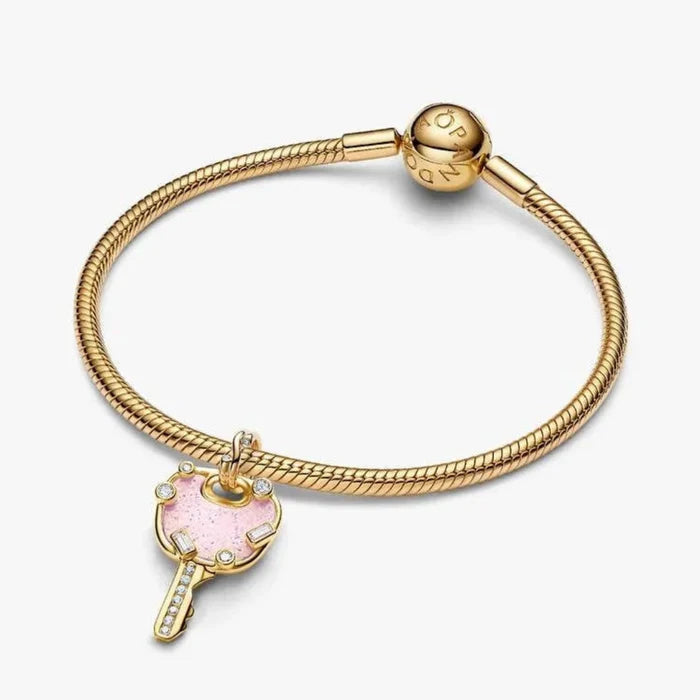 Gold bracelet with a pink heart charm on a white background
