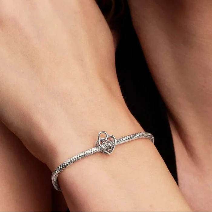 Silver bracelet with a heart charm on a wrist against a neutral background