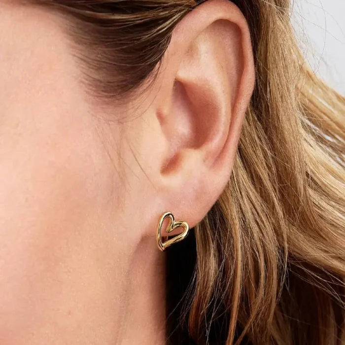 Pandora heart-shaped hoop earrings in gold tone worn on a woman’s ear.