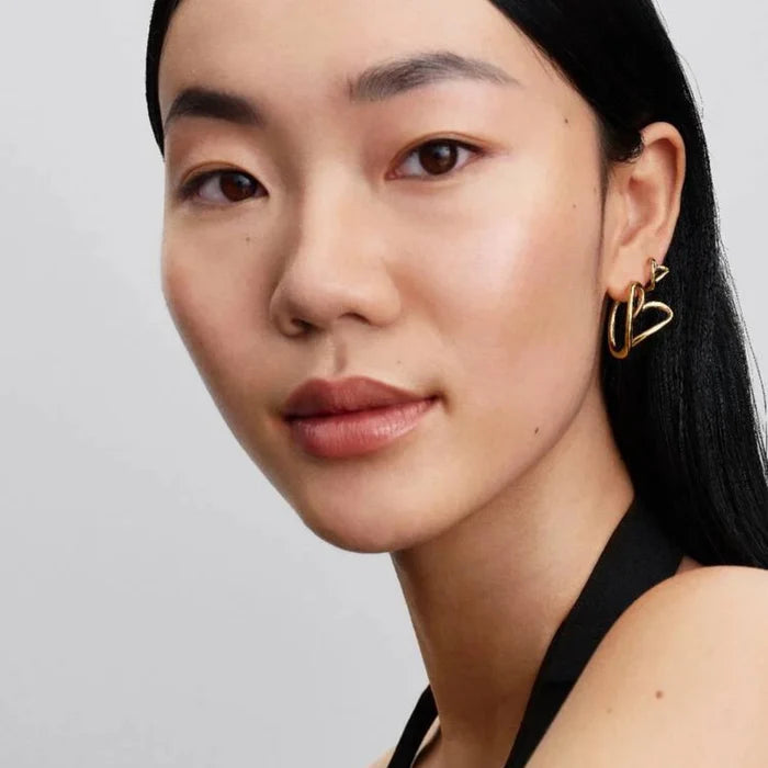 Woman wearing the Pandora Organically Shaped Heart Hoop Earrings in gold tone on her ear.