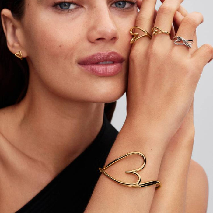 Woman wearing the gold-tone Pandora Organically Shaped Heart Small Ring on her finger, along with other heart rings and a heart bracelet.