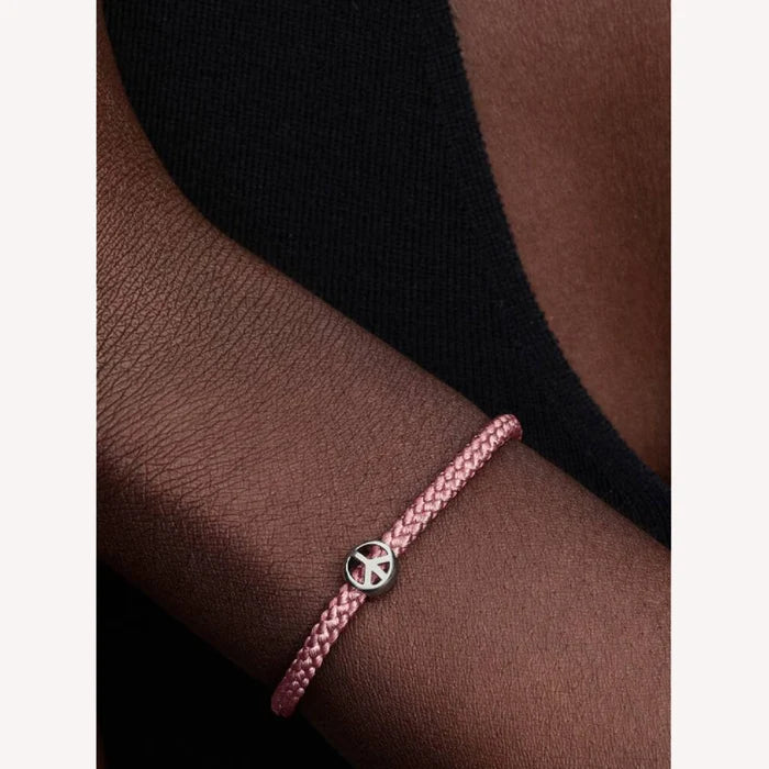 Pink braided bracelet with a silver peace symbol charm on a wrist